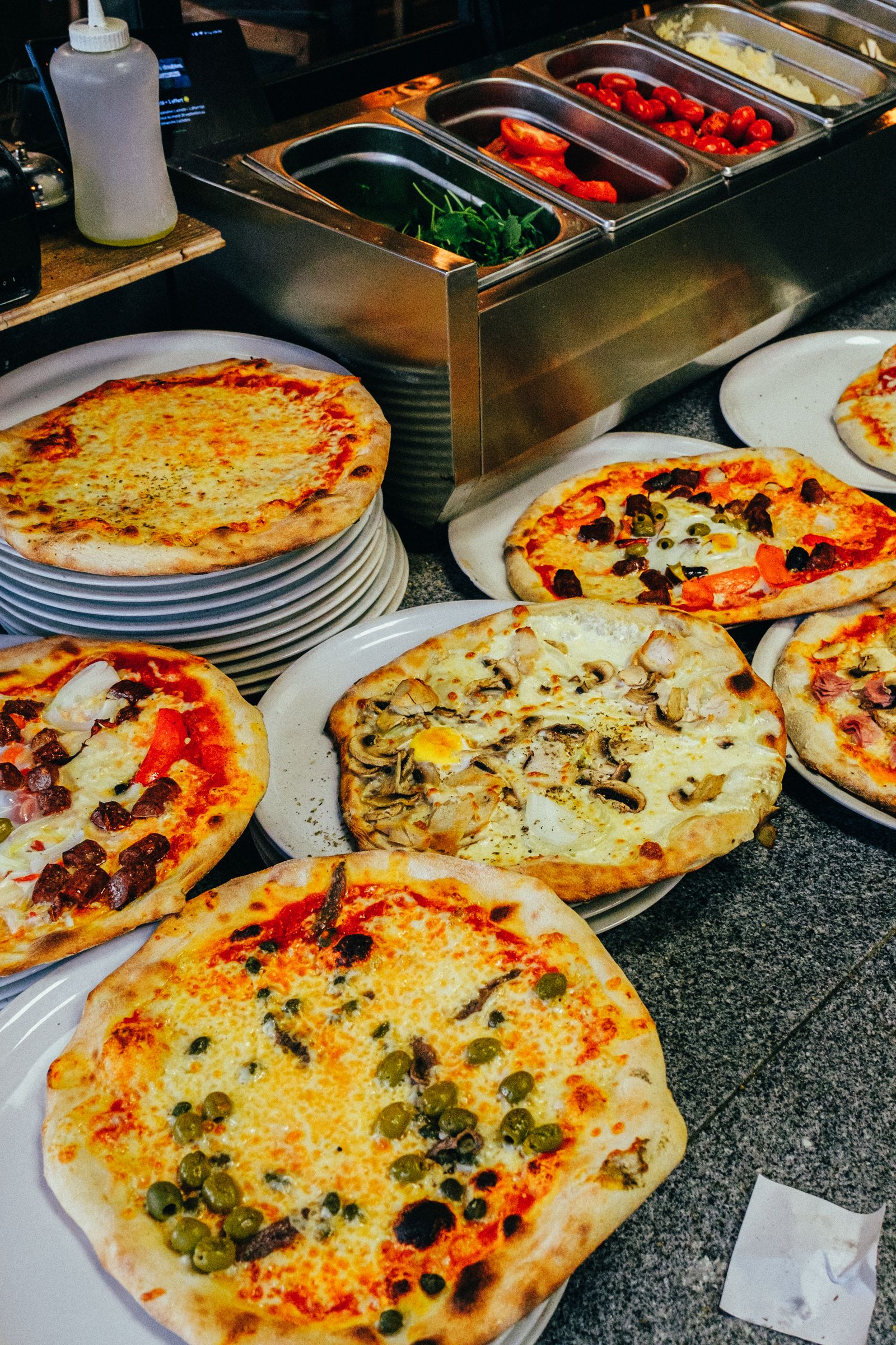Balcão de pizzaria com várias pizzas prontas em pratos